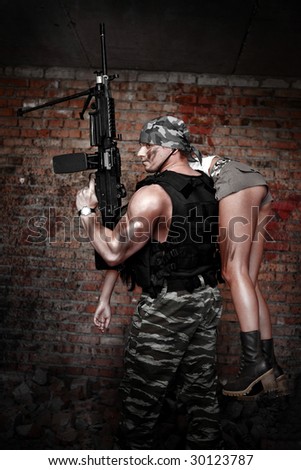 Armed man with light machinegun with the pretty girl on the shoulder on the ruined building back?round.