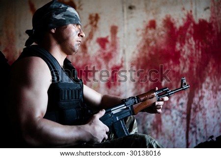 Armed mercenary with \'Kalashnikov\' submachine gun on the bloody wall background