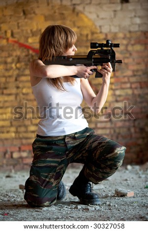 Armed woman with the rifle on the brick wall background.