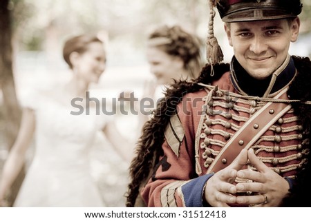 Smiling hussar in vintage outfit. Two pretty women on the background are discussing him.