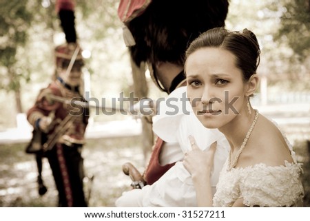 Portrait of pretty woman dressed in vintage dress and accessories. Dueling hussars on the background. Focus point on the girl.