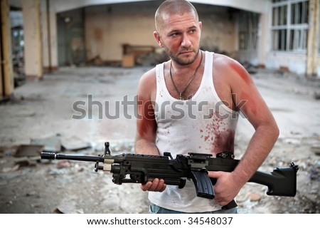 Armed rebel in bloody t-shirt with machinegun on the ruined building background.