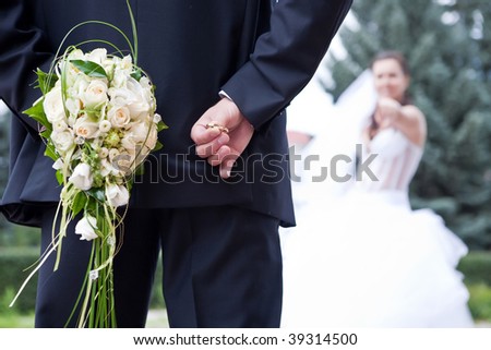 Bridal game. Groom is holding bridal rings in the one hand and bride\'s bouquet in the other. Bride is trying to guess.