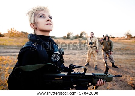 Blond woman with rifle. Two rebels with Kalashnikov machine gun on the background.