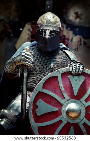 Medieval knight in the armor with the sword and shield. Portrait in the shadows.