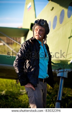 Smoking pilot in the helmet in front of vintage plane