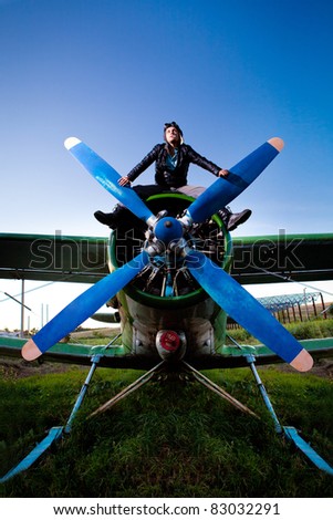 Crazy pilot is sitting on the plane\'s engine. Rural background.
