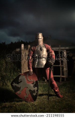 Medieval knight in the armor with the sword and shield. Sunset on the background.