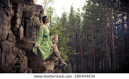 Elf woman is sitting on the rocks. Forest on the background.