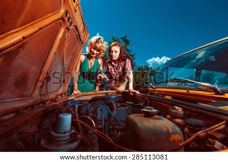 Beautiful woman mechanic is repairing a car another woman is watching.