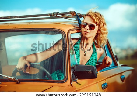 Woman is driving an old yellow car. Rural background.