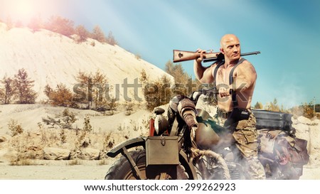 Muscular bald biker with the rifle. Apocalypse background. Instagram-like toning.