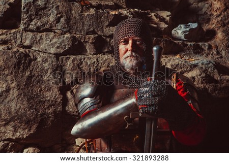 Old medieval King in armor with sword on the rocks background. Focus point on the face.