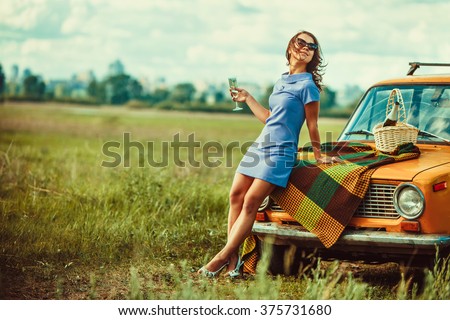 Beautiful woman on the picnic is drinking wine near a car.