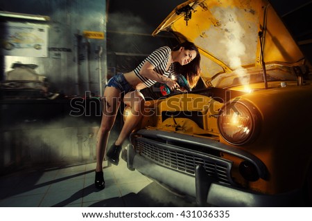 Woman mechanic in sexy shirts is repairing an old car with the screwdriver.