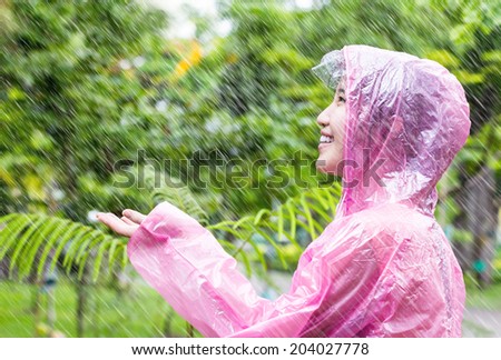 Asian woman in pink raincoat enjoying the rain in the garden