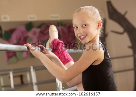 Little ballerina girl with leg on bar in dance studio