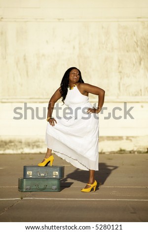 African American woman with suitcases waits and laughs outside an industrial building.