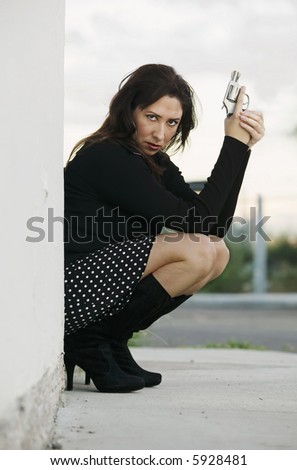 Hispanic woman behind a wall holding a handgun in ready to fire position.