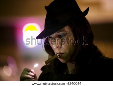 Woman in a fedora lighting a cigar with a match.