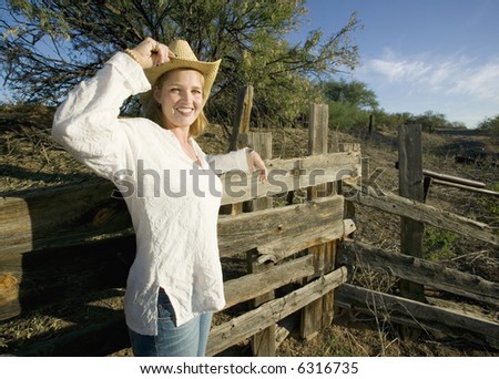 Western woman leans against a decrepit old split rail fence.
