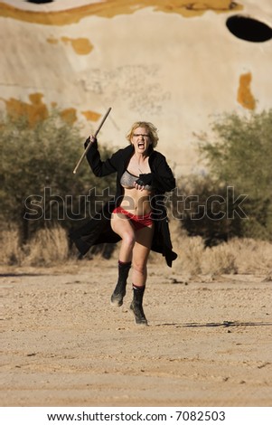 Female science fiction model in a desolate location attacking with a wooden stick.