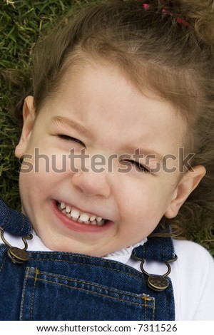 Little girl laying in the grass making a silly face with a big smile.