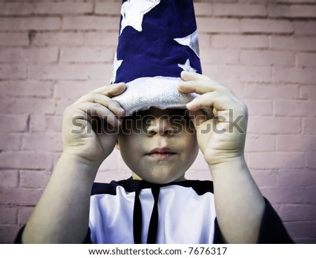 Young boy lifts the brim of a wizard hat and peers out.