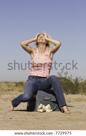 Blonde woman sitting on suitcases and laughing.