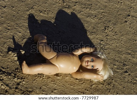 Abandoned child\'s baby doll with blue eyes on parched desert dirt.