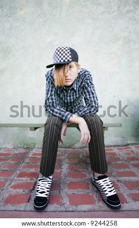 Teenage boy with crazy hair and a clothes on a green bench.