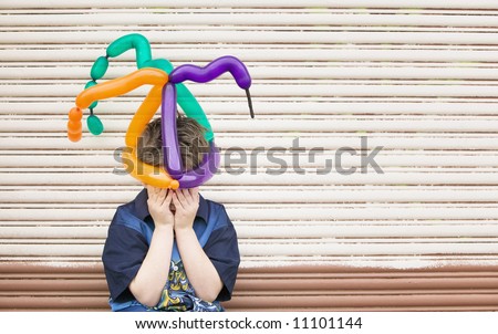 Young boy wearing a balloon hat hides his face