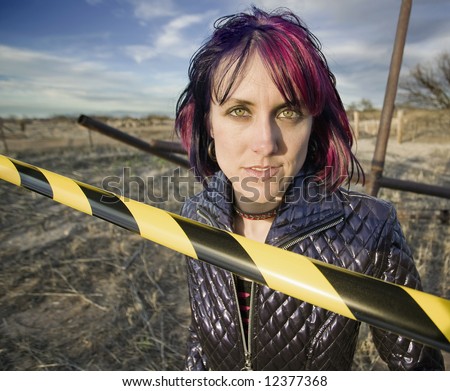 Punk girl outdoors behind a strip of yellow and black caution tape