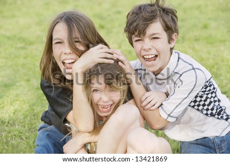 Three young siblings wrestling outdoors on the grass