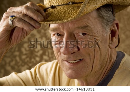 Senior man tipping a straw hat in front of gold wallpaper