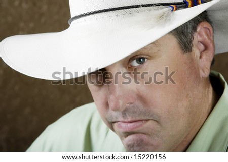 Man beneath a white cowboy hat in front of a gold background