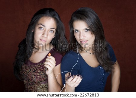 Two pretty Hispanic women sharing a headset listening to music