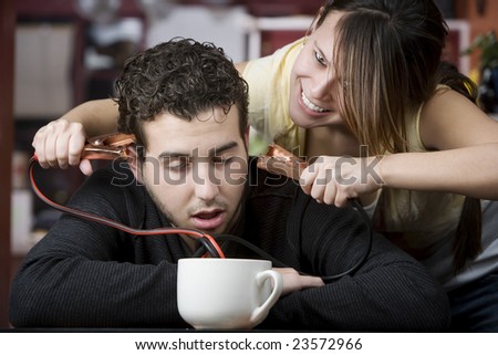 Young woman holding jumper cables coming out of coffee mug to man\'s head