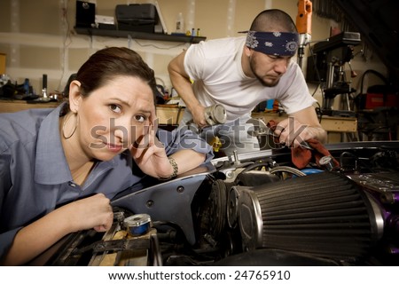 Bored woman leaning on car with male mechanic ignoring her in background