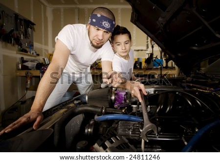 Hispanic father and son working on car engine in garage