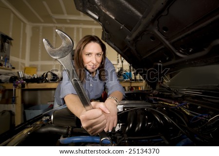 Pretty Hispanic woman with wrench working on car in garage