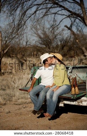 Man and woman in cowboy hats kissing on back of pickup truck