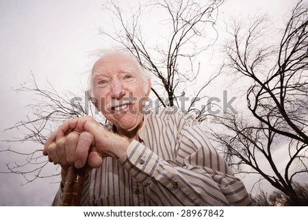 Crazy old man leaning on cane in front of trees
