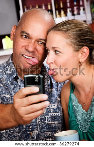 Attractive couple in a coffee house taking self-portrait with cell phone