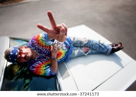 Hippie on the hood of car making peace sign