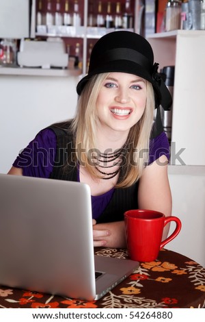 Smiling blonde girl with laptop and mug at a cafe
