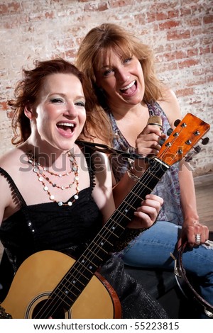 Female musicians sing along with guitar in front of a brick background