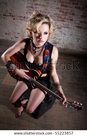 Female punk rocker with her guitar in front of a brick background