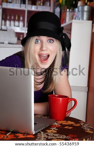 Surprised blonde girl with laptop and mug at a cafe