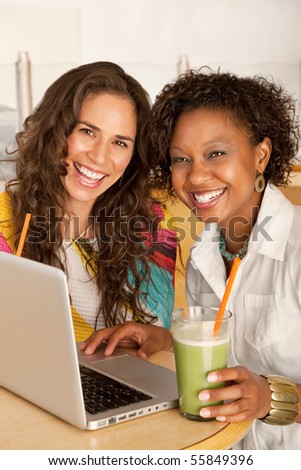 Two women are working on a laptop while enjoying smoothies.  Vertical shot.